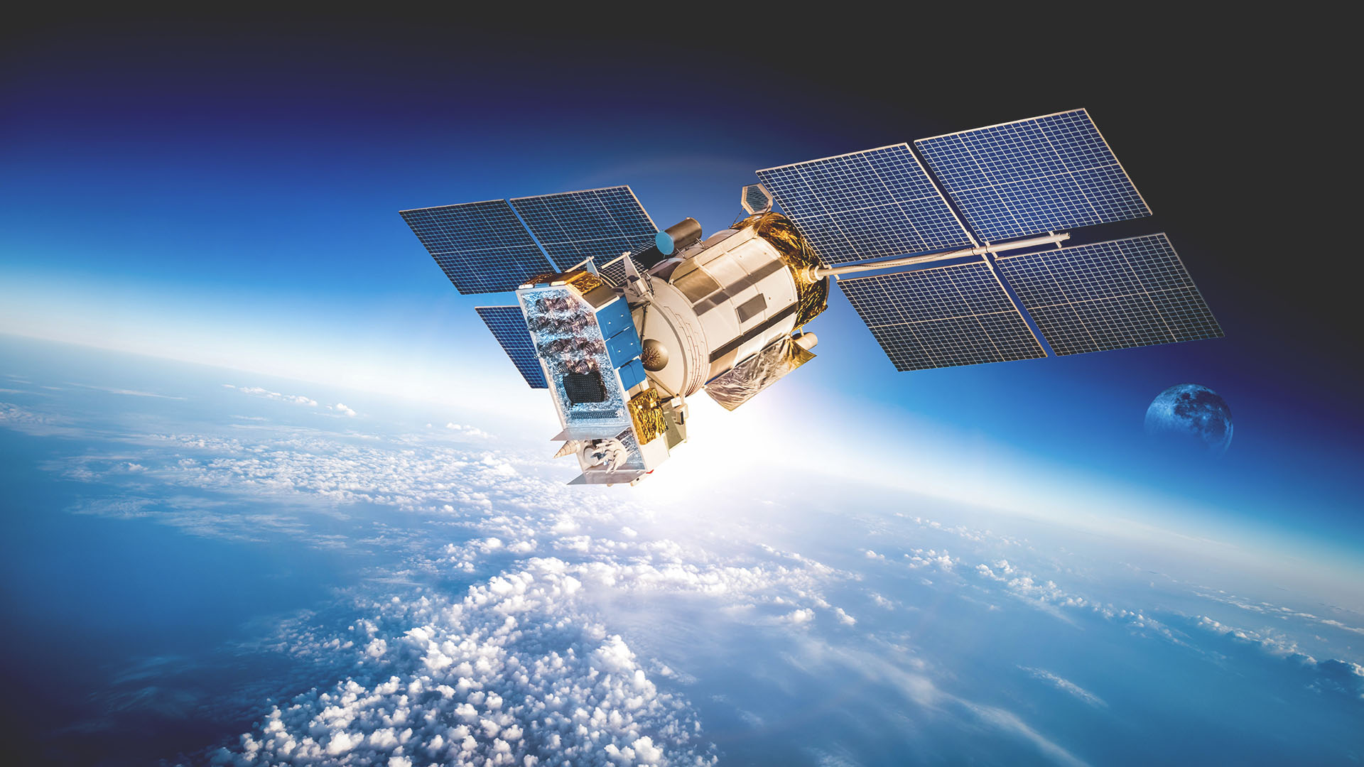 A satellite in space with its solar wings open and the moon visible on the earth’s curved horizon