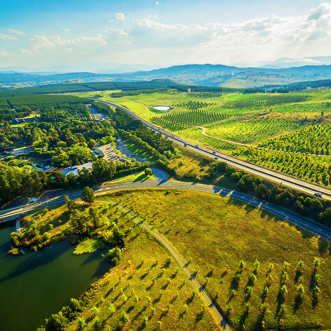 Aerial image of a landscape that includes a field and hills with green trees, ponds, and roads