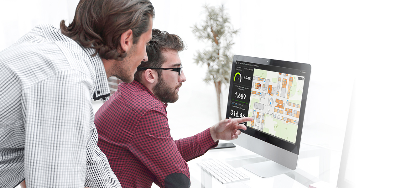 Due uomini che guardano lo schermo di un computer che mostra una mappa blu e rosa che rappresenta i dati GIS per la pianificazione dello spazio interno