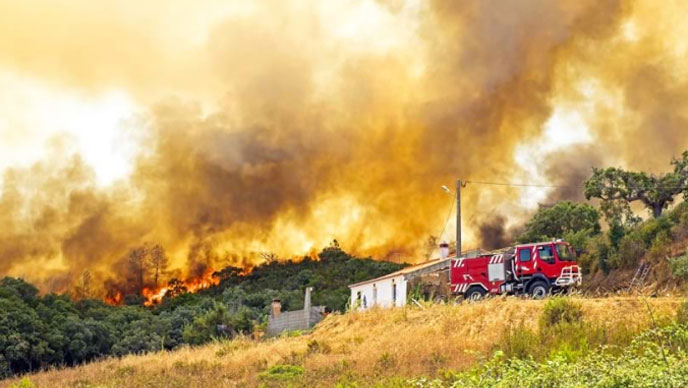 Un campo verde erboso con colline di vegetazione con fiamme arancioni e fumo nero