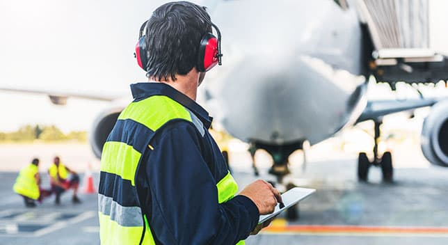 Ispettore aeronautico che indossa le cuffie dell'aviazione e tiene una tavoletta che ispeziona un aeroplano