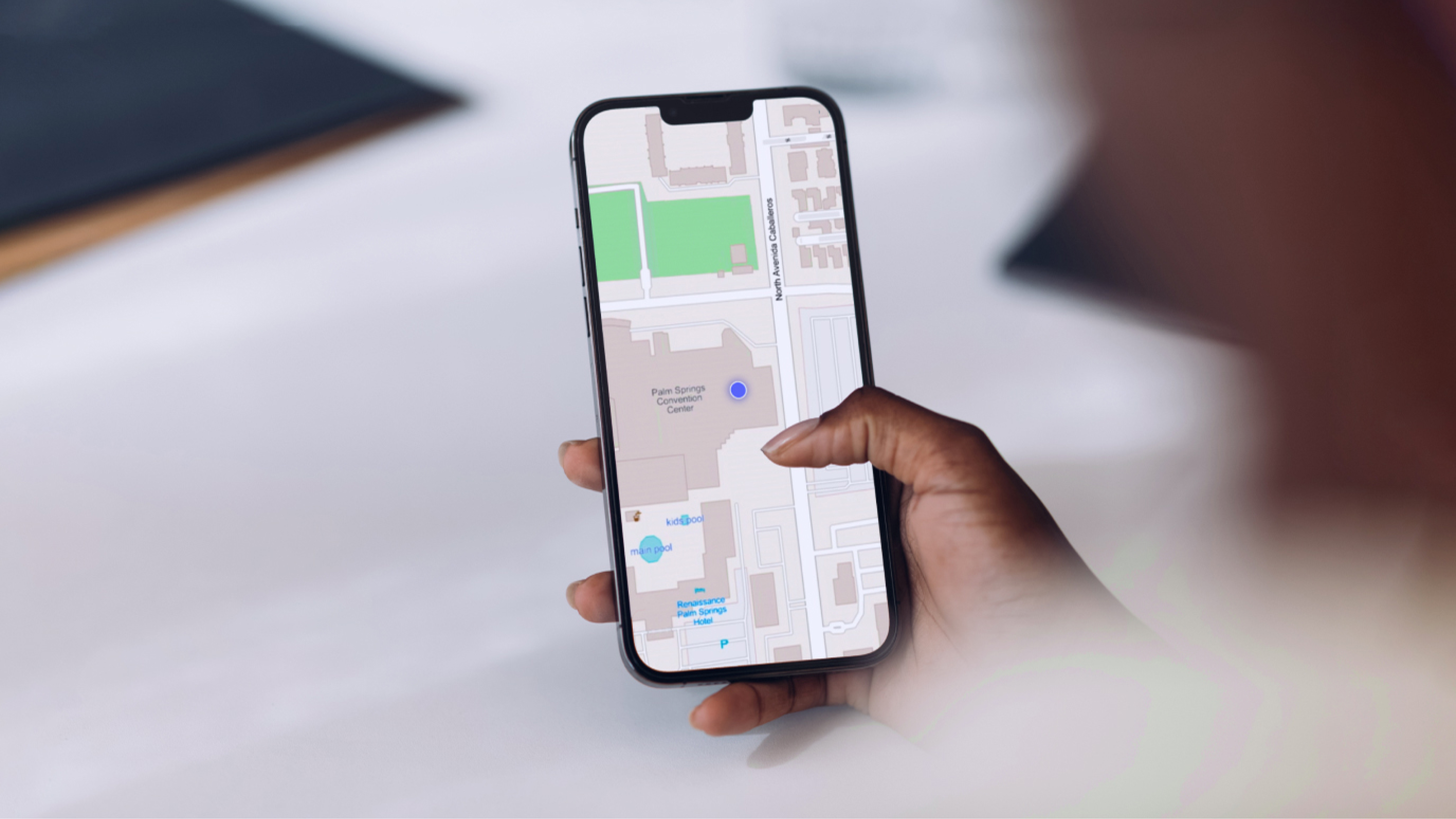 Una mano che tiene un telefono cellulare che mostra una mappa grigio chiaro con un pennarello blu su uno sfondo sfocato