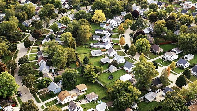 Immagine aerea di una grande area residenziale piena di alberi lungo strade curve con graziose case bianche e prati verdi