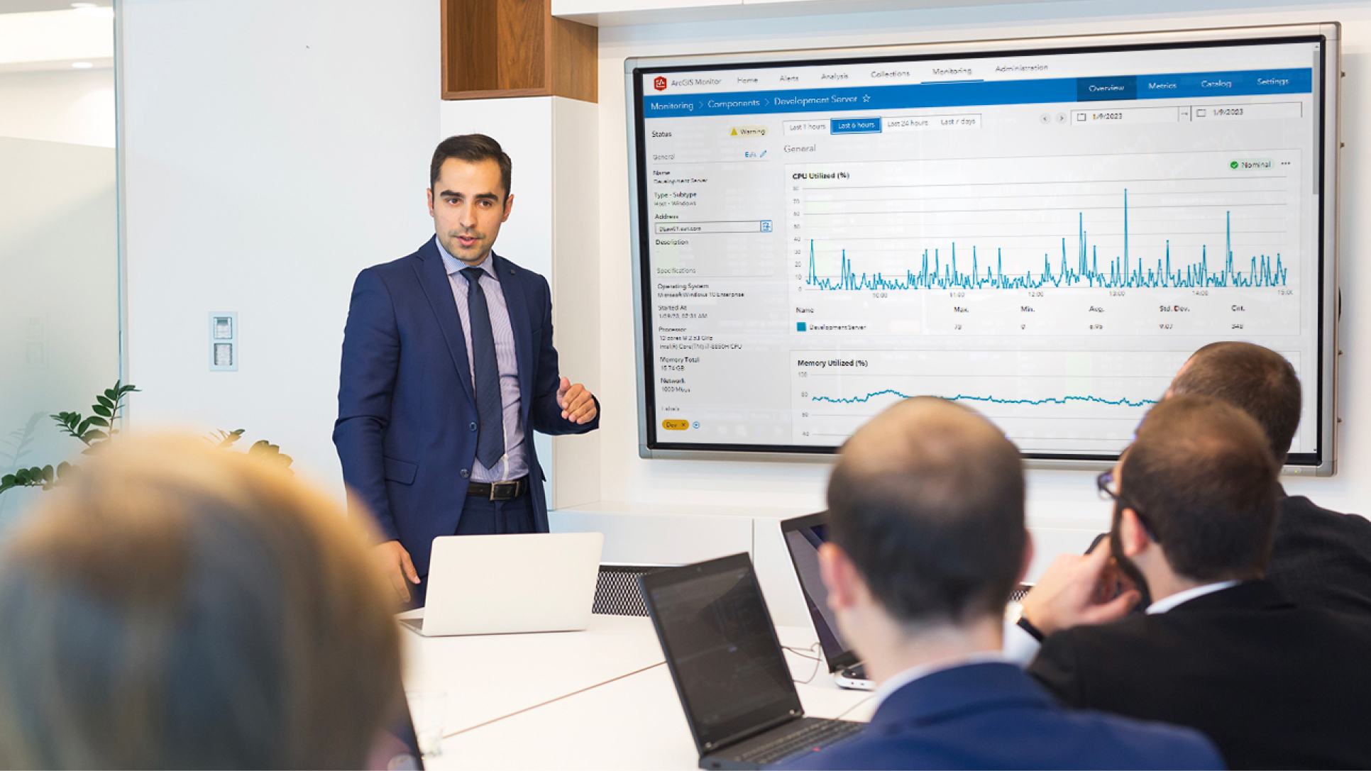 Un gruppo di persone in una sala conferenze con un'altra persona accanto a un grande monitor che visualizza un grafico