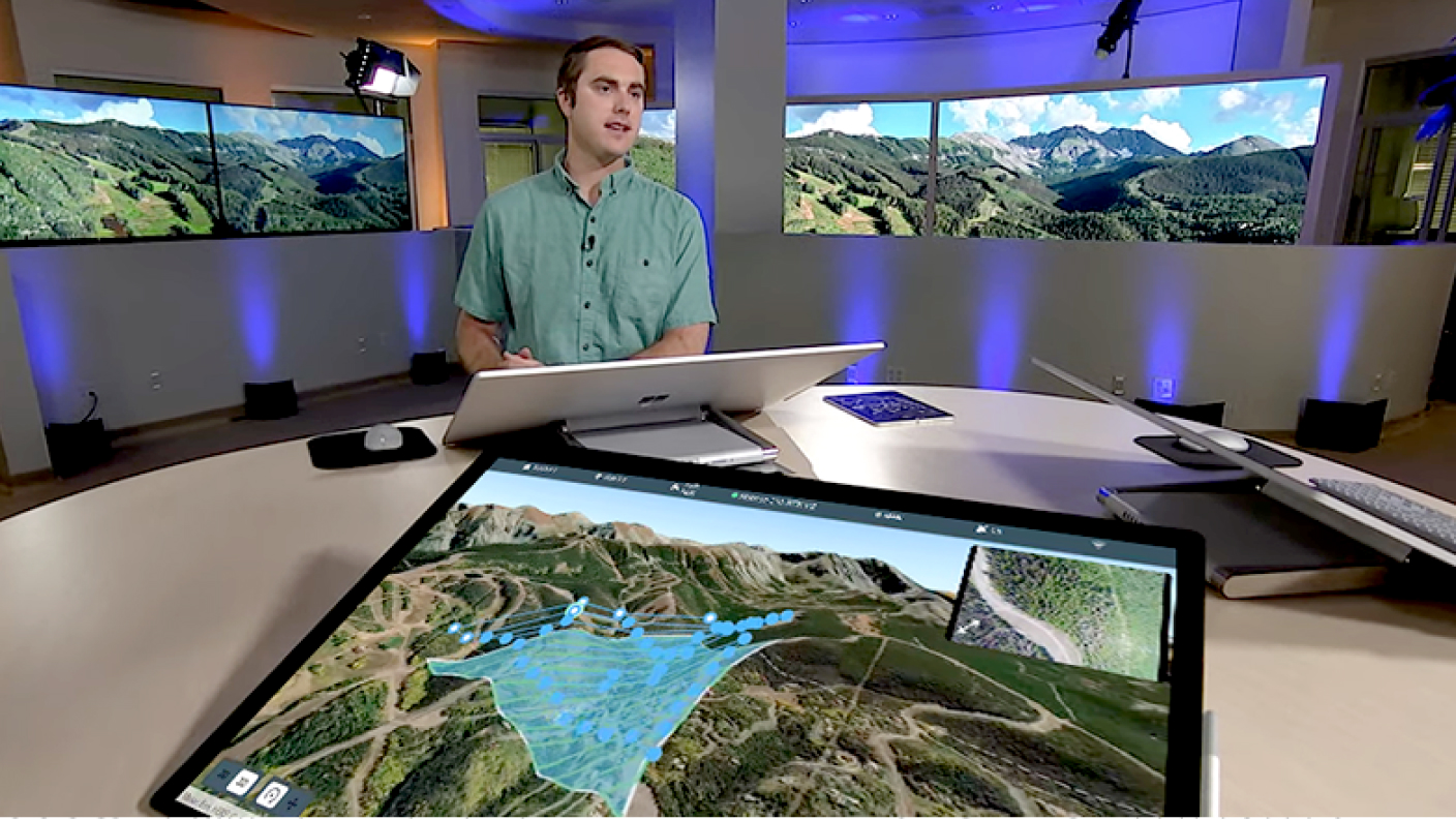 Uomo in piedi accanto a un grande tavolo rotondo davanti a un grande monitor di computer con 2 grandi monitor tv che mostrano un'immagine digitale 3D