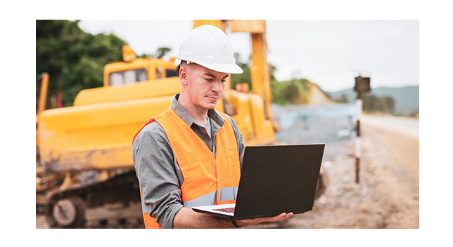 Lavoratore edile con un laptop in un cantiere con un bulldozer sullo sfondo