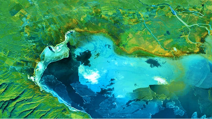 A stunning aerial image showcasing a vibrant coastal region with a mix of green terrain and bright blue water.