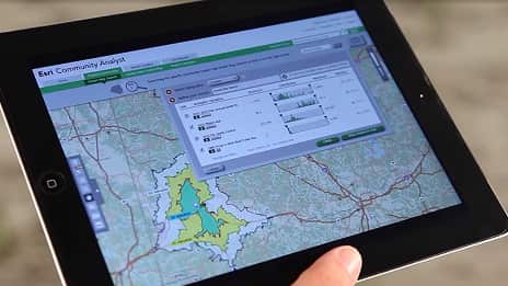 A person's hand hovers over an iPad screen displaying a map and data interface with a prominent play button