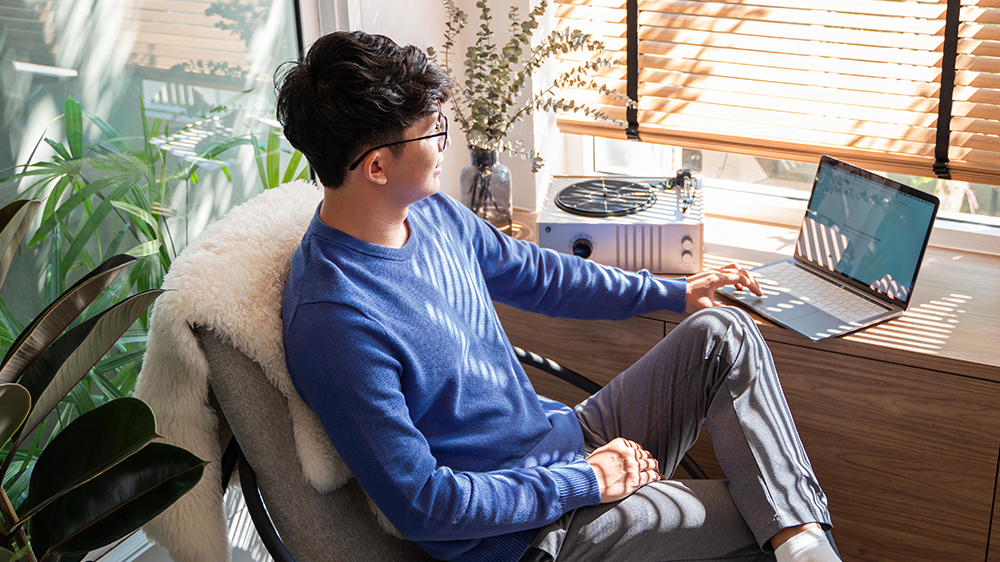 A person sitting cross-legged at his desk browsing on his laptop